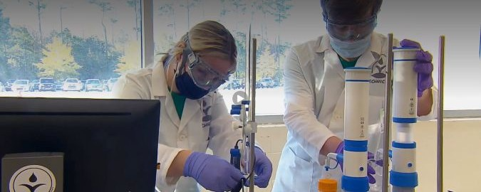 Two students are working on equipment in a lab at Blythewood High School to make biodiesel out of used cooking oil. Students are wearing safety glasses, masks, and gloves.